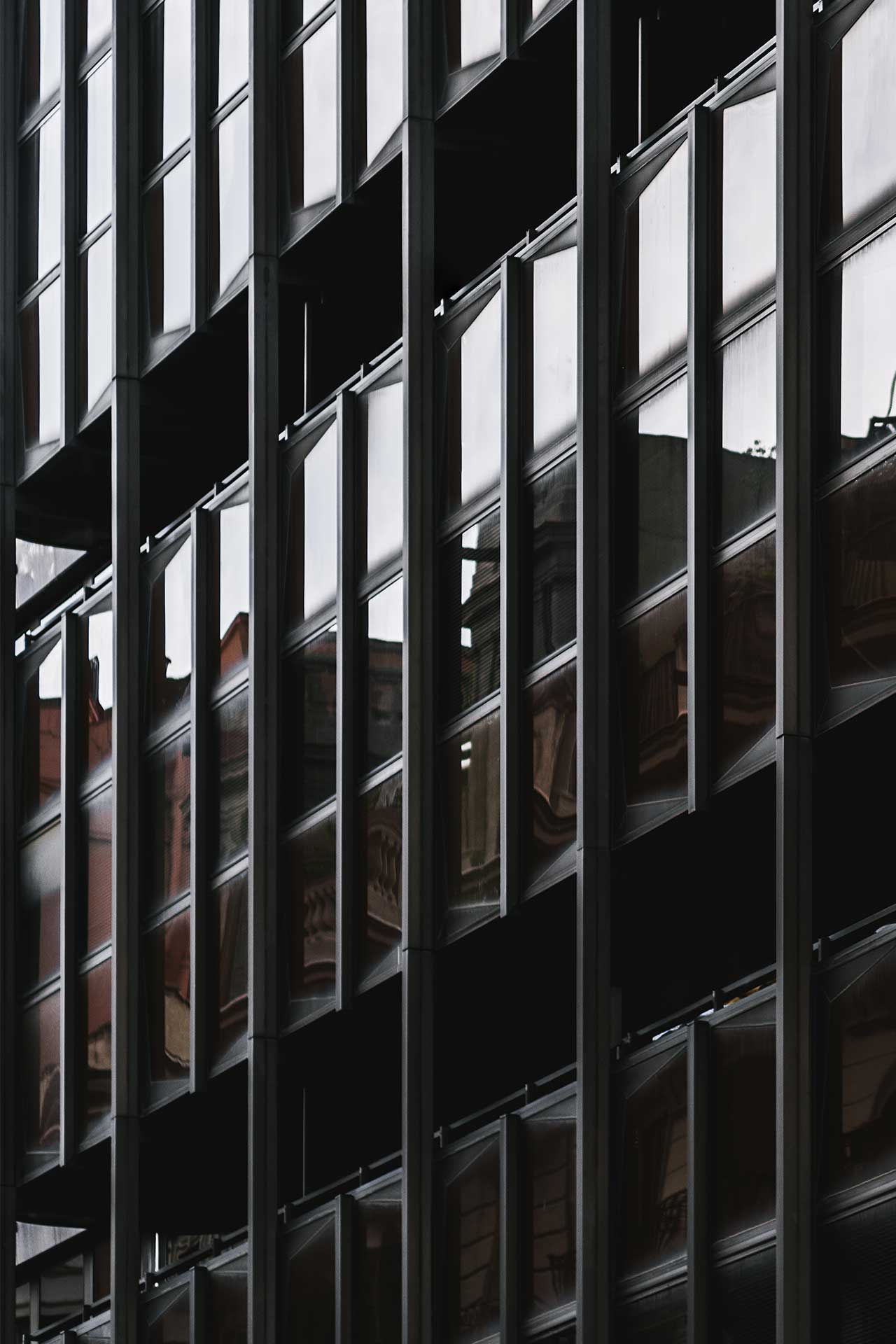 Close-up of a modern building's façade featuring dark glass windows reflecting surrounding architecture.