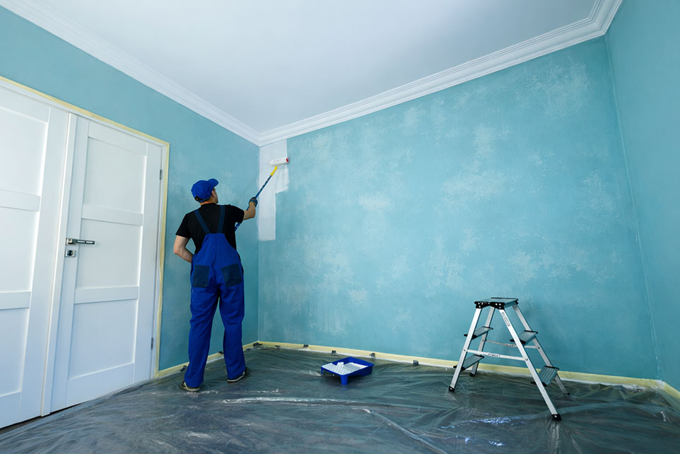 Interior painting contractor applying fresh paint over uneven and faded blue walls.