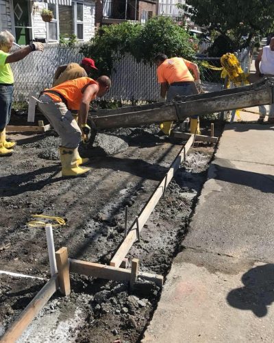 Construction workers are actively repairing a sidewalk, using tools and materials for the project.