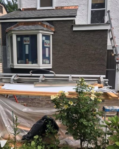 A house being painted, with a ladder leaning against it and another ladder placed on top of the roof.