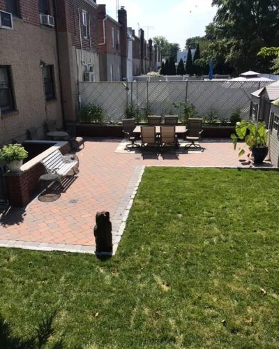 A backyard featuring a patio with lawn furniture, surrounded by a well-maintained green lawn.