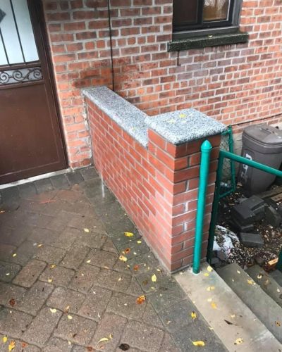 A brick wall featuring a green railing and a matching green door.