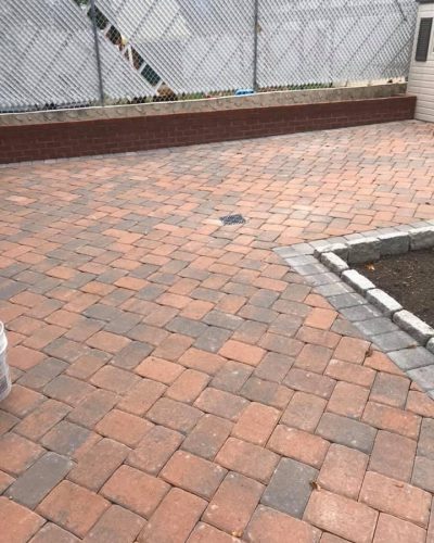 Paved area featuring a pattern of rectangular bricks in shades of orange and gray, bordered by a low stone wall.