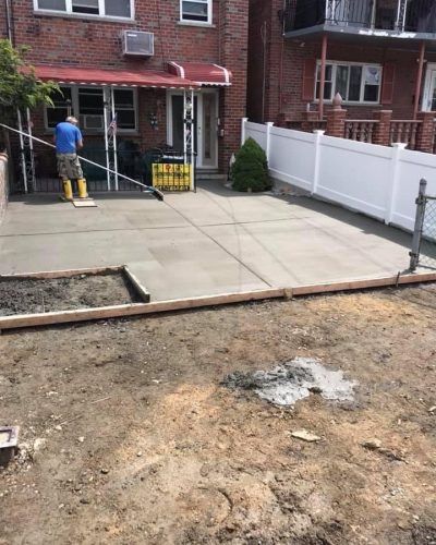 Concrete patio installation in Brooklyn, showcasing workers laying concrete slabs in a residential outdoor space.