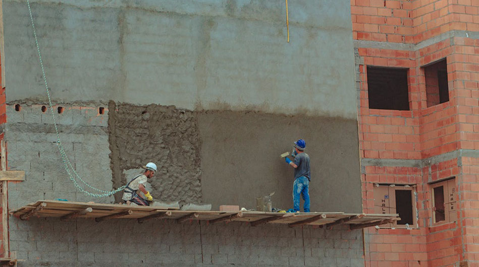 Construction workers in hard hats and safety vests are actively working on a building site, using tools and equipment.