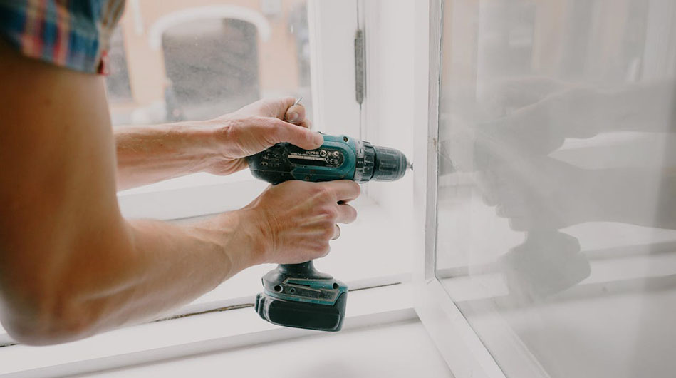 A man repairs a window using a drill, focused on securing the frame with precision and care.